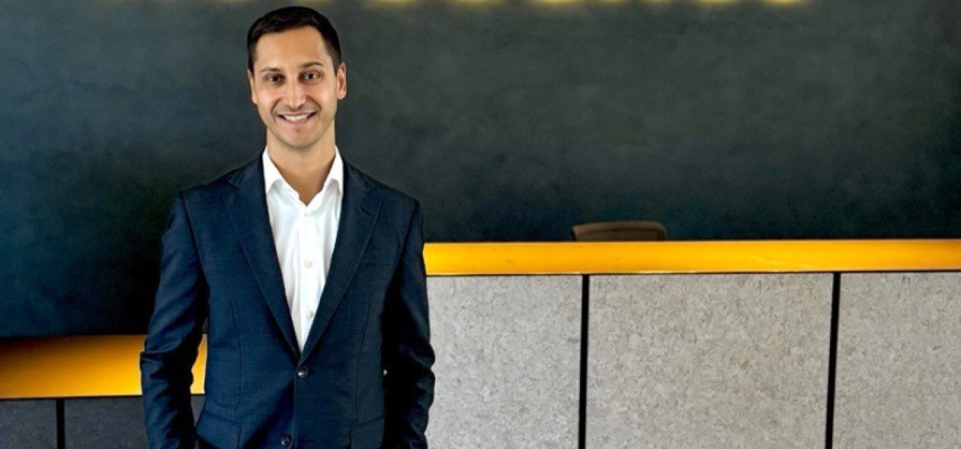 Colaborador novobanco de fato e mãos nos bolsos a sorrir com o logo logotipo por trás